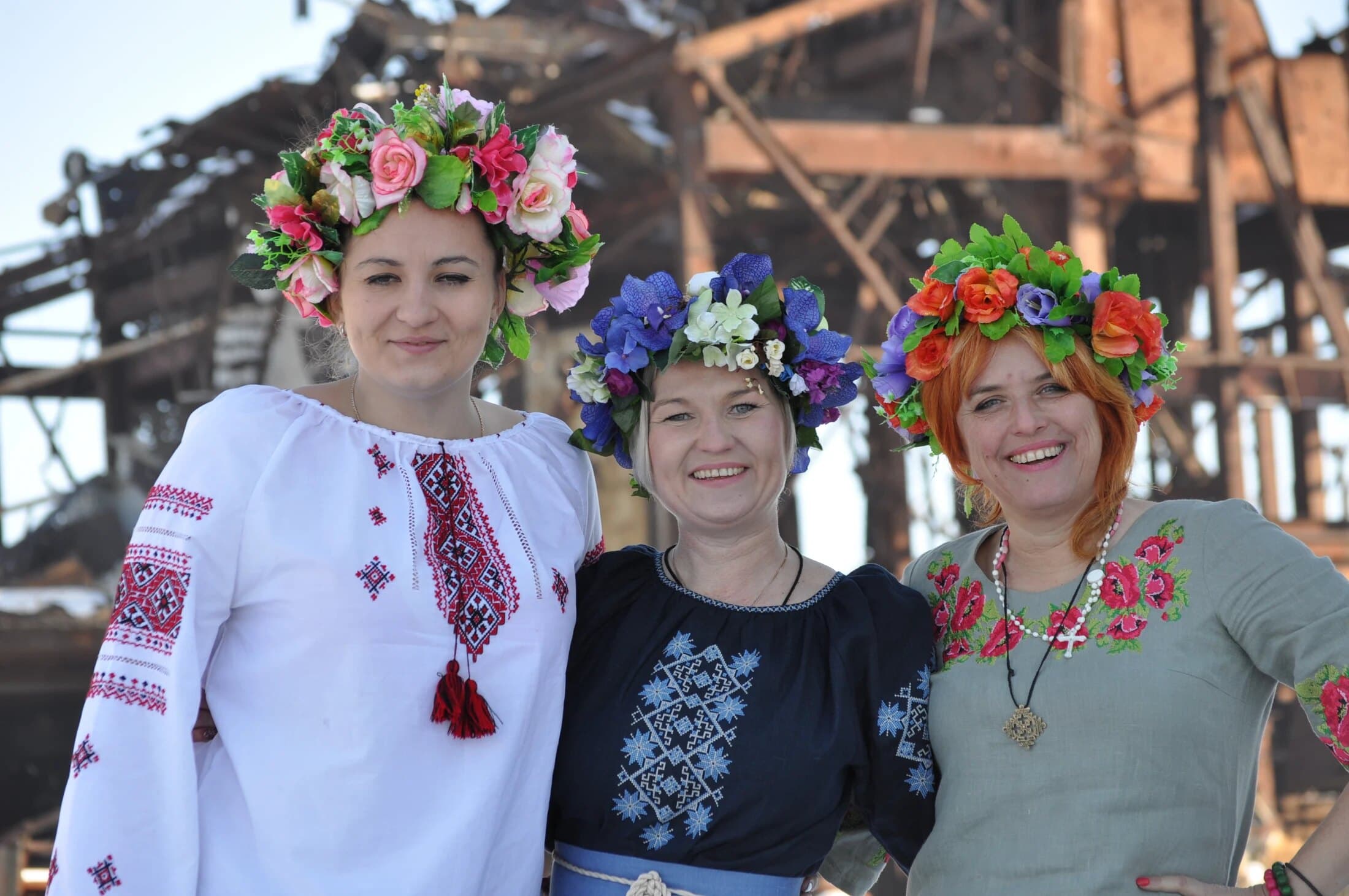 Three women in embroidered blouses and flower crowns, smiling together
