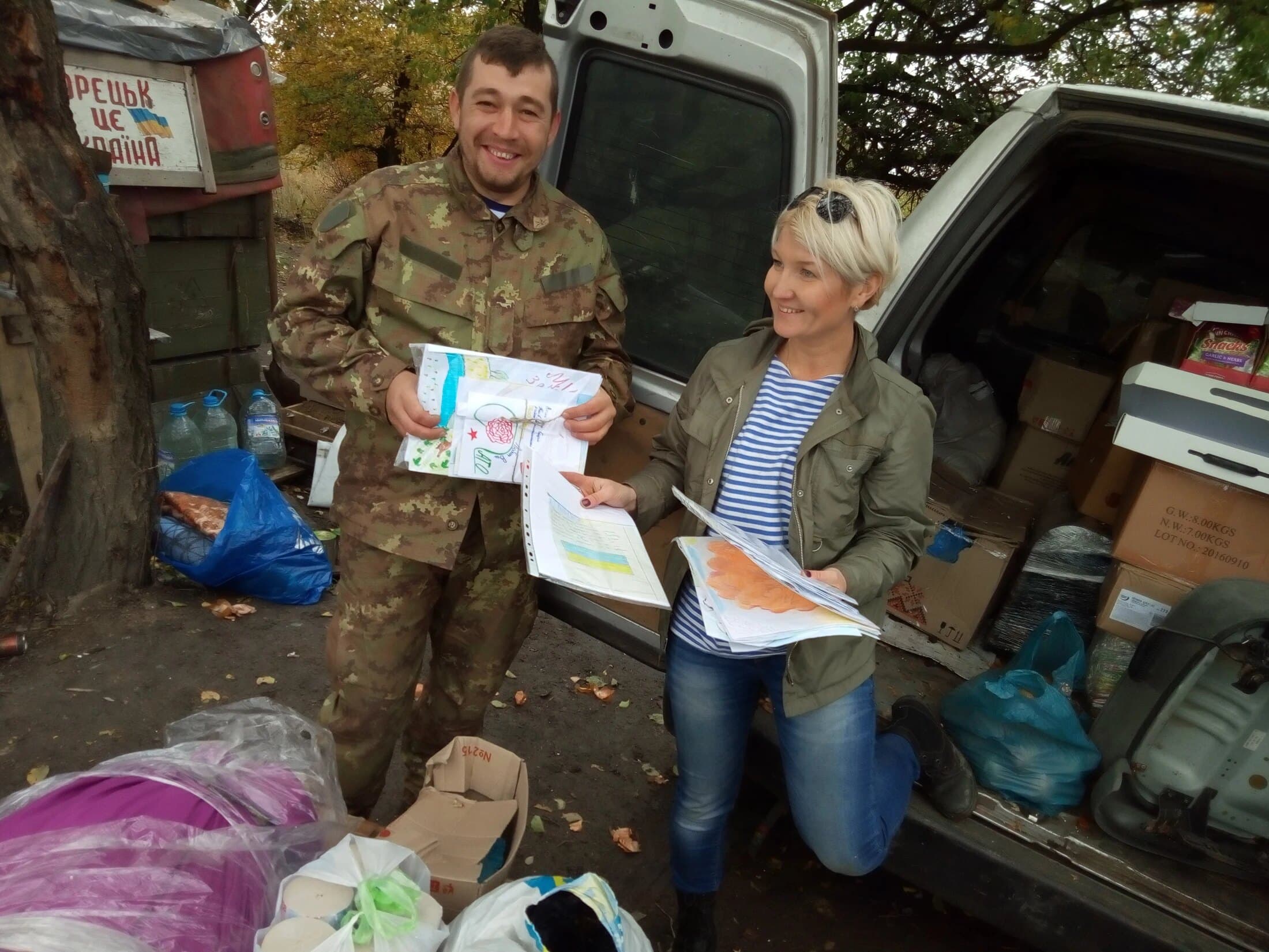 Natalka kneeling by an open van, sorting medical supplies with a volunteer