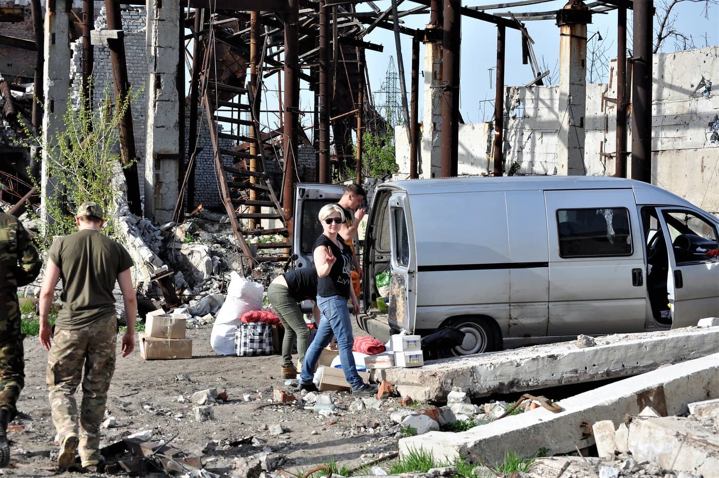 Volunteers unloading boxes of supplies from a van among ruined buildings