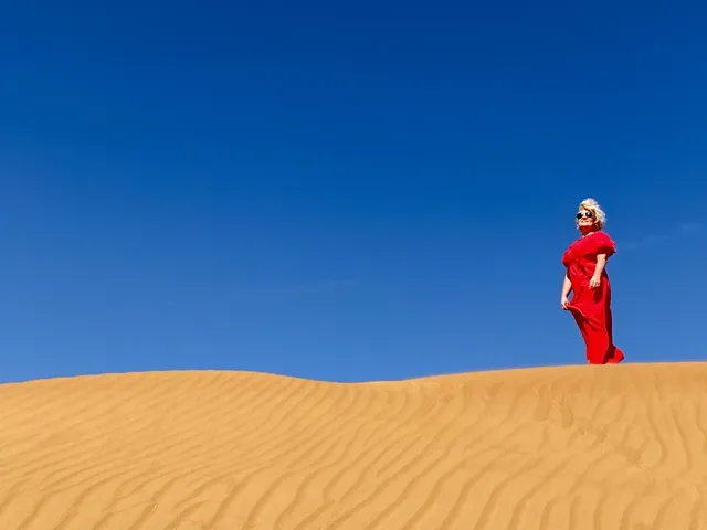 A person in red standing on a golden dune under a blue sky